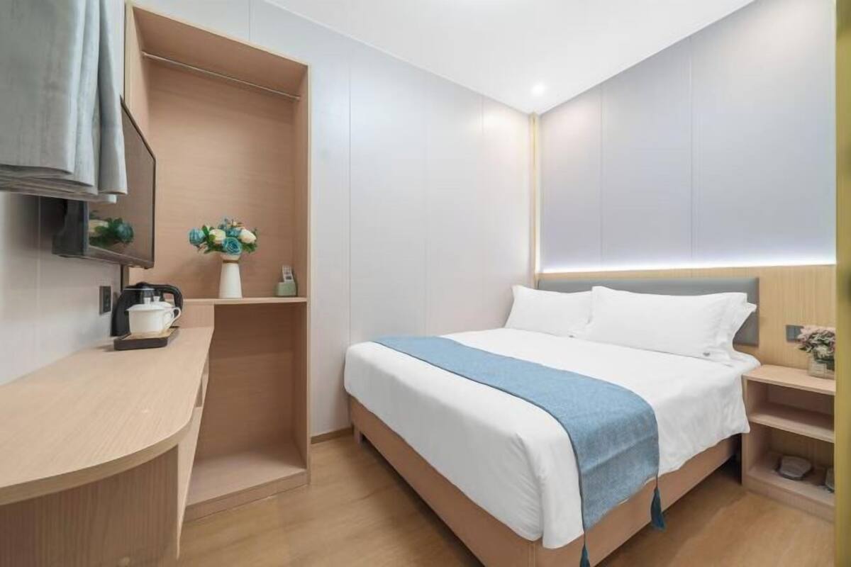 Una habitación de hotel moderna con una cama, una mesita de noche, un estante empotrado con un jarrón de flores y un televisor de pantalla plana montado en la pared.