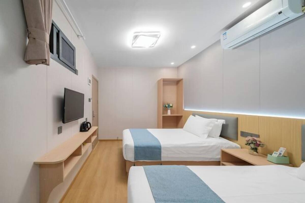 Habitación de hotel con dos camas, televisión, escritorio y mesita de noche con lámpara.