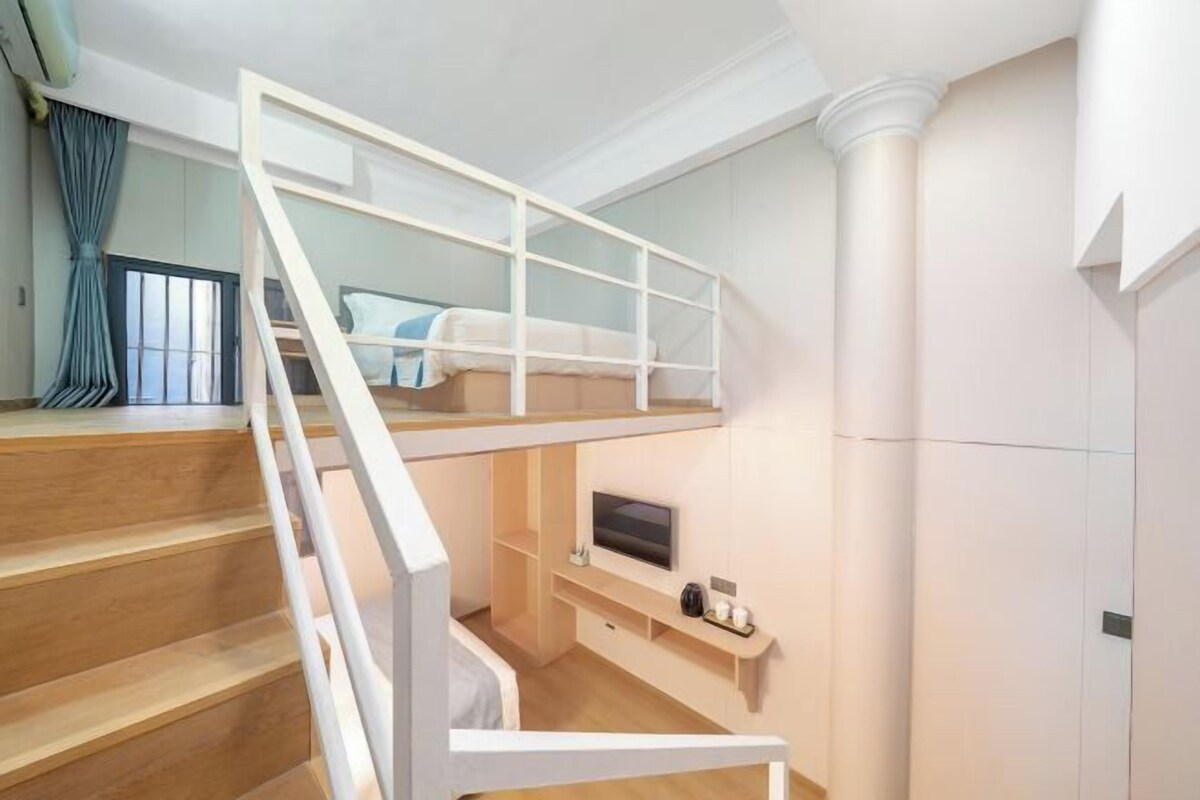Ein modernes Zimmer mit einer Holztreppe, einem Bett, einem Fernseher und einem kleinen Regal.