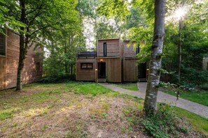 Eine moderne Holzblockhütte mit einer zentralen Tür und Fenstern, umgeben von einem bewaldeten Gebiet.