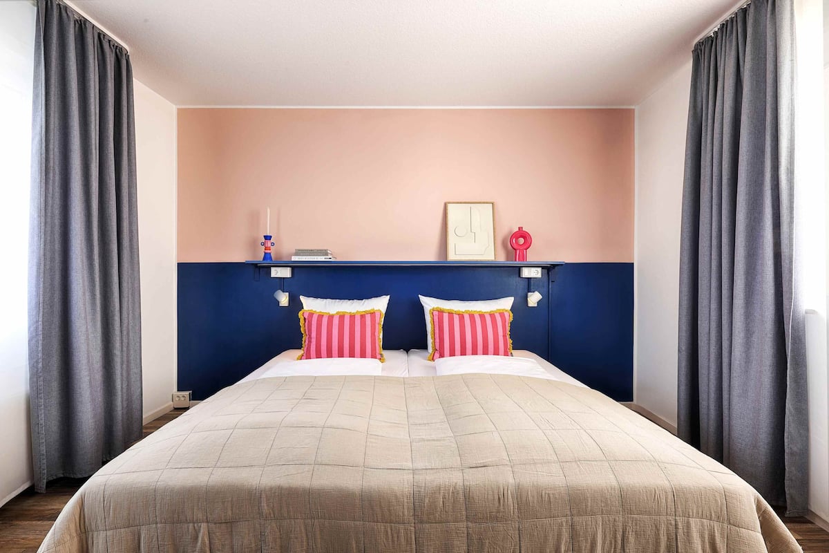 A double bed with a beige bedspread and two pillows with pink and white stripes.