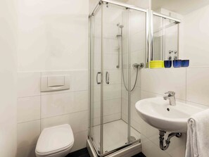 Een moderne badkamer met een douche met glazen wand, een wit toilet en een wastafel met een spiegel erboven.