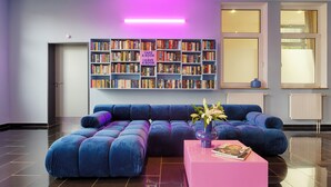 A modern living room with a large bookshelf, a blue sectional sofa, and a pink coffee table. - homie hotel max apart (Fuerth)