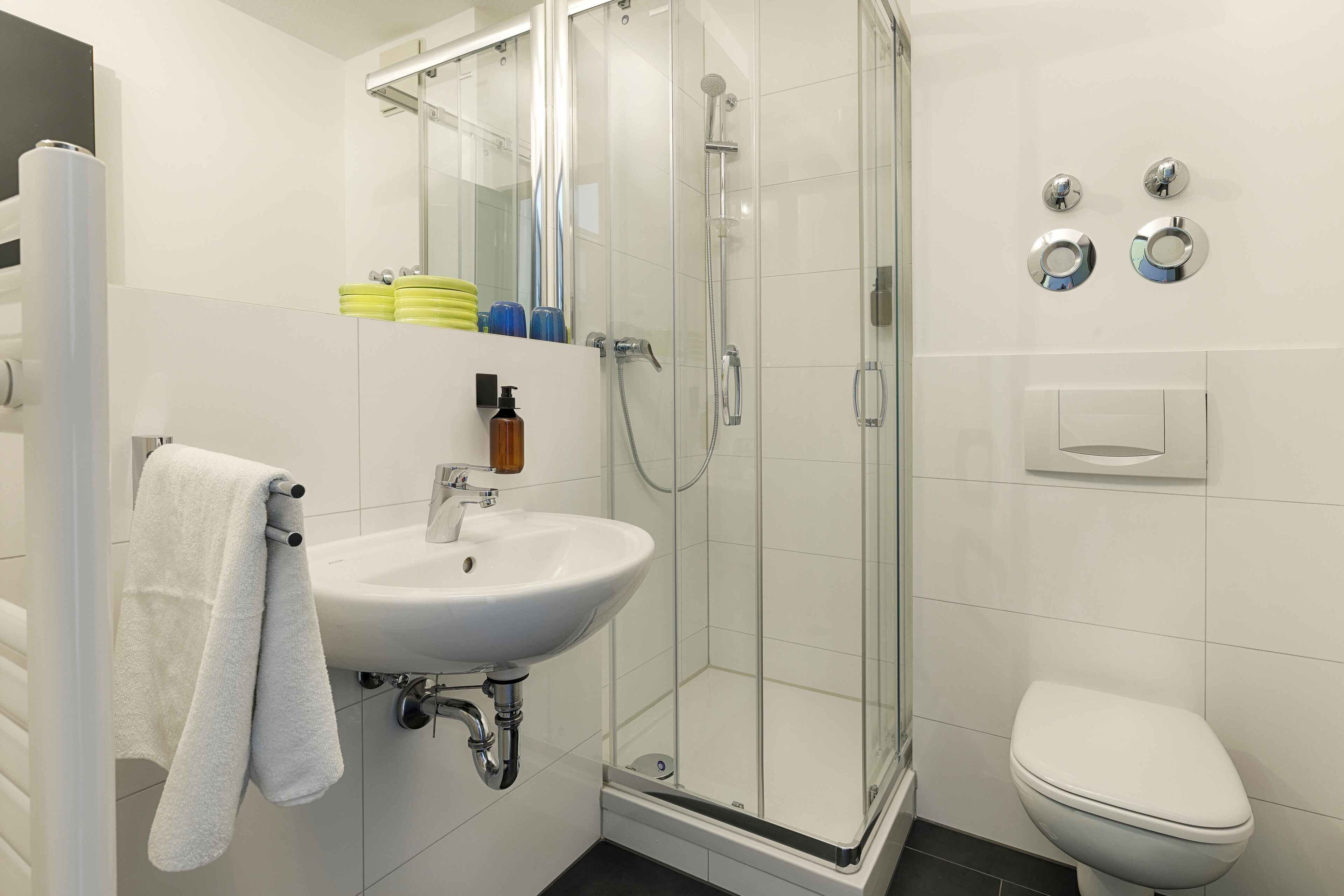 A modern bathroom with a glass-enclosed shower, a white sink, and a toilet.
