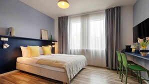 A modern bedroom with a bed, a desk, and a TV. - homie hotel max apart (Fuerth)