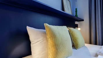 Un lit bien fait avec deux oreillers, un mur bleu et une étagère sur laquelle se trouvent un tableau et une bougie.