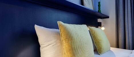 A neatly made bed with two pillows, a blue wall, and a shelf with a picture and a candle.