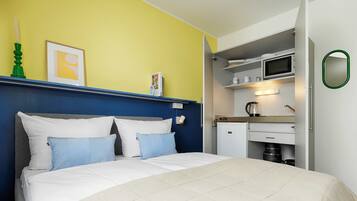 A bedroom with a bed, pillows, a bedside table, a wall-mounted clock, and a framed picture.