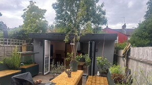 A wooden deck with a table and benches, surrounded by potted plants and a small garden area. - Inviting 1-bed Studio in London (London)