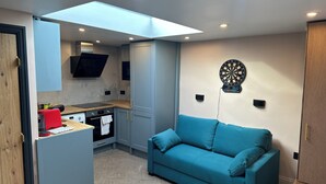 A compact living space with a kitchenette, a blue sofa, and a dartboard on the wall. - Inviting 1-bed Studio in London (London)