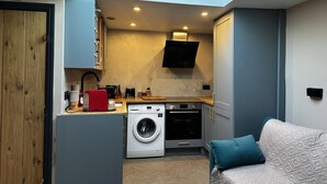 A compact kitchen with a built-in washer, a small dining area, and a sofa with a teal pillow. - Inviting 1-bed Studio in London (London)