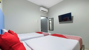 Ein Hotelzimmer mit zwei Betten, roter und weißer Bettwäsche, einer Klimaanlage, einem Flachbildfernseher und einer Tür zu einem weiteren Raum.