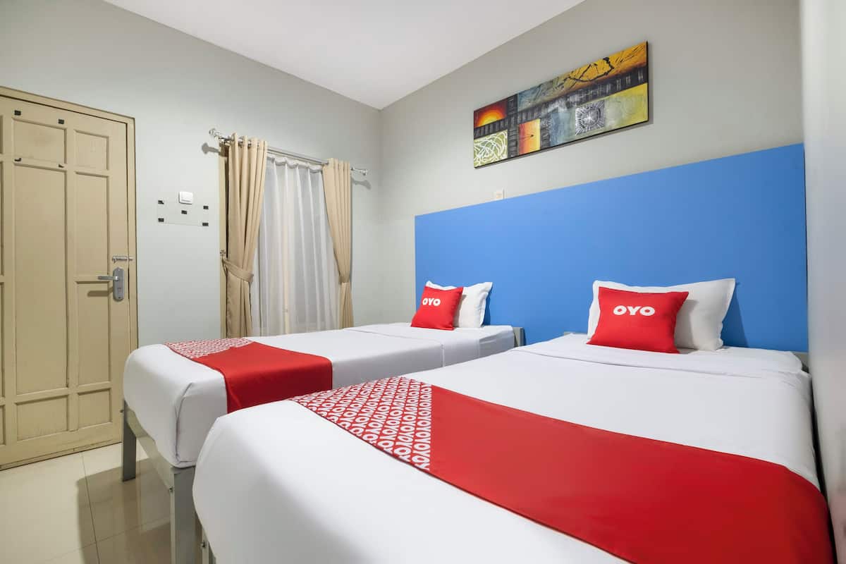 Une chambre d’hôtel avec deux lits, chacun recouvert d’une couvre-lit rouge et blanche, et agrémenté d’oreillers assortis.
