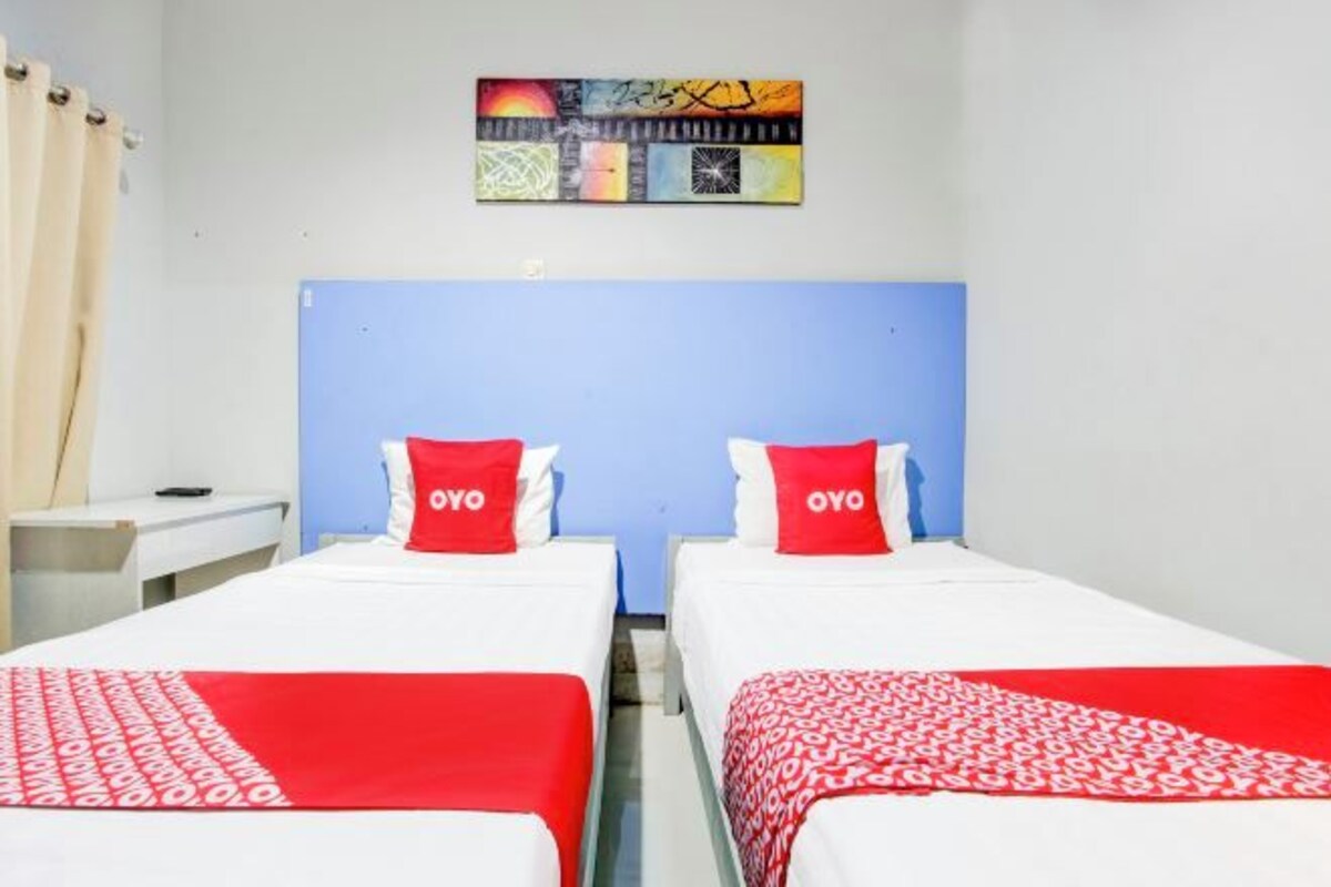 Une chambre d’hôtel avec deux lits, chacun recouvert d’une courtepointe rouge et blanche, assortie aux coussins.