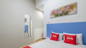 A hotel room with a bed, a painting of flowers, a mirror, and a sign on the nightstand. - Hotel O Prawirotaman Near Keraton Yogyakarta Formerly Paris Guesthouse (Sewon)