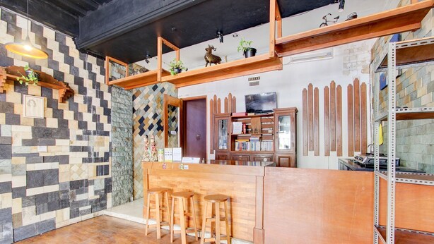 A reception area with a wooden counter, stools, a television, and a wall with a checkered pattern. - Hotel O Prawirotaman Near Keraton Yogyakarta Formerly Paris Guesthouse (Sewon)