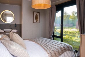 Ein Schlafzimmer mit einem großen Bett, einem runden Spiegel, einem Waschbecken und einem Fenster mit Blick ins Grüne.
