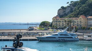 A large yacht docked at a marina with a backdrop of a cliff and buildings. - Sunlight Properties - Capitaine 54 - 1 Bed rental apartment, balcony, port view (Nice)