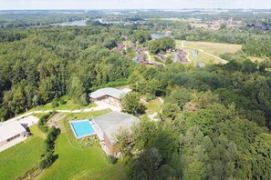 An aerial view of a resort with a swimming pool, tennis courts, and a large building with a flat roof.