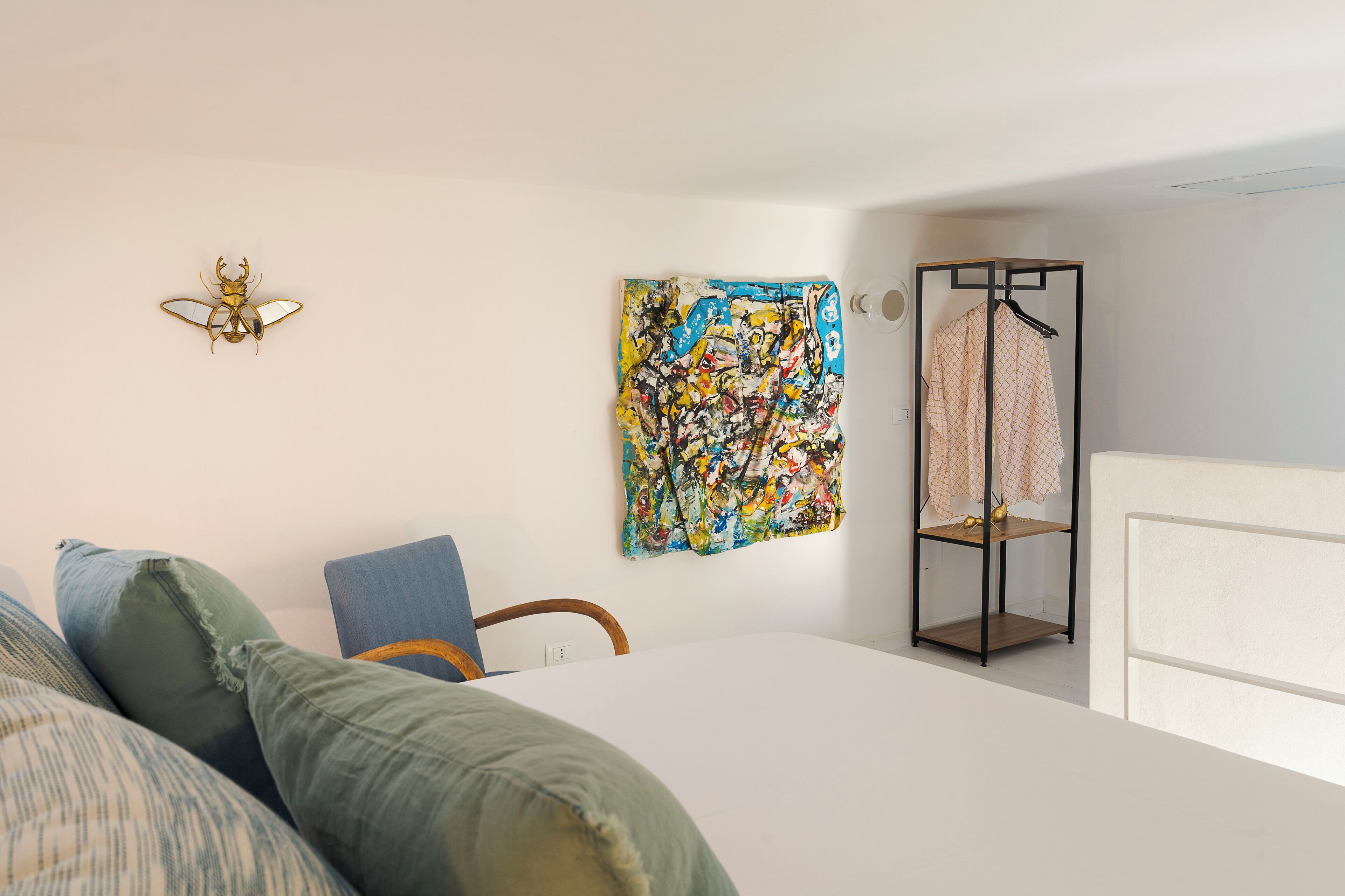 A bedroom with a bed, pillows, a wall art piece, a clothing rack, and a small table.