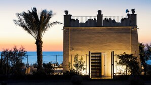 A building with a gated entrance, a palm tree, and a view of the sea at sunset. - Tower of the 7 friars - Tower in Cefalu with direct access to the beach (Cefalù)