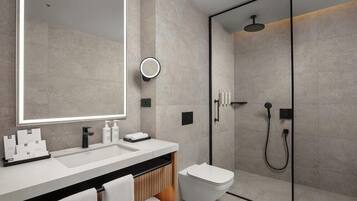 A modern bathroom with a large mirror, a sink, a toilet, and a glass-enclosed shower area.