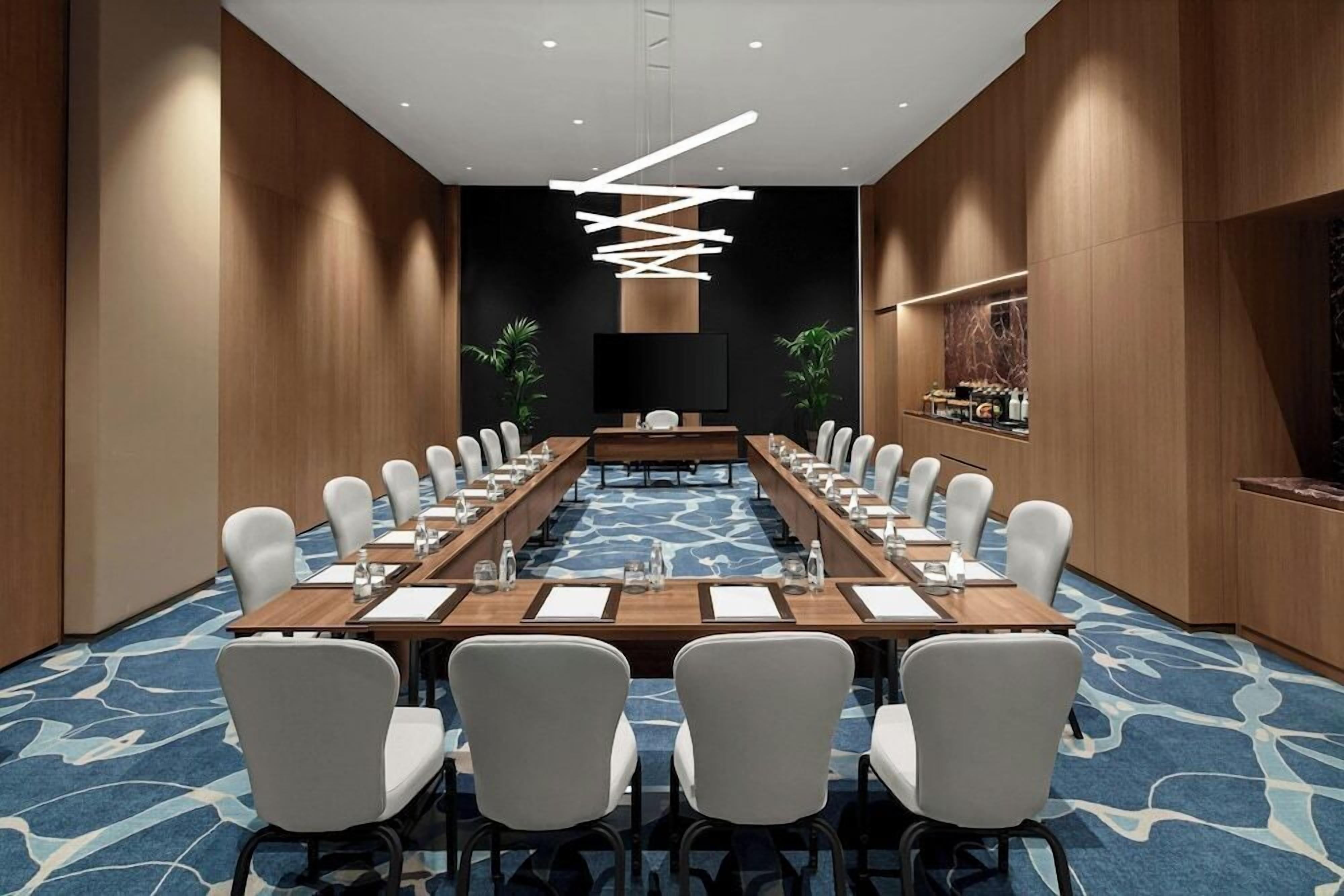 A conference room with a long table, chairs, a flat-screen TV, and a modern light fixture.