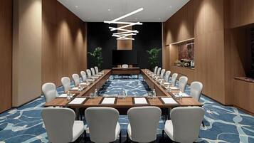 A conference room with a long table, chairs, a flat-screen TV, and a modern light fixture.