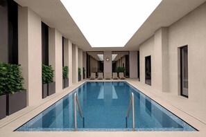 A modern indoor swimming pool with a skylight, surrounded by walls with large windows and potted plants.