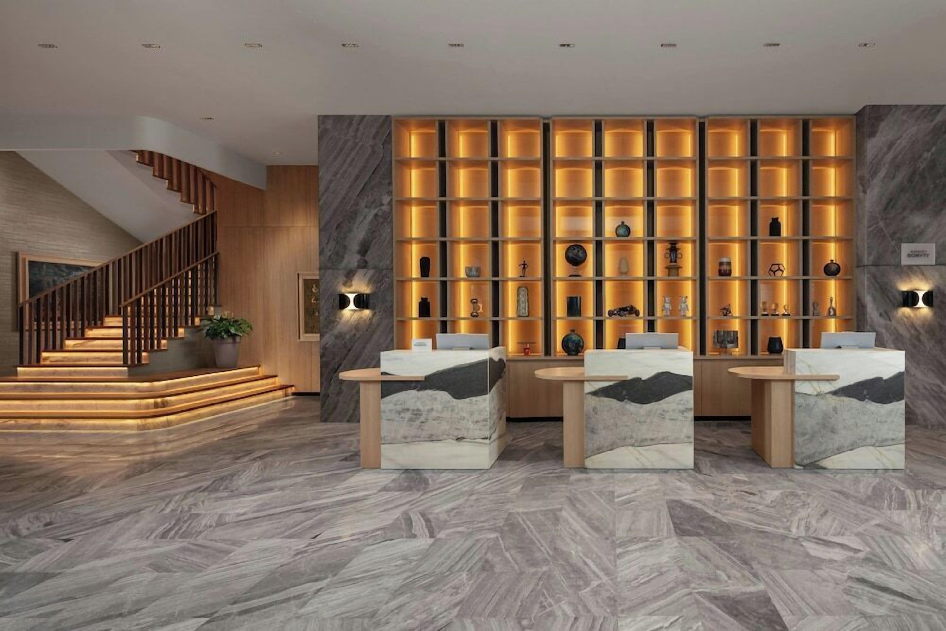 Eine moderne Lobby mit Marmorboden, einer Treppe und einer Wand mit beleuchteten Regalen.