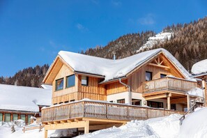Chalet-style building with a spacious balcony and pitched roof, set amidst snow-covered mountains.