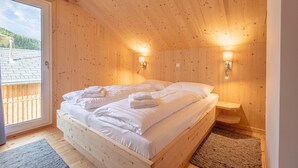 Ein Schlafzimmer in einer Holzhütte mit einem Bett, zwei Wandleuchten und einem Fenster mit Blick auf eine Holzterrasse.