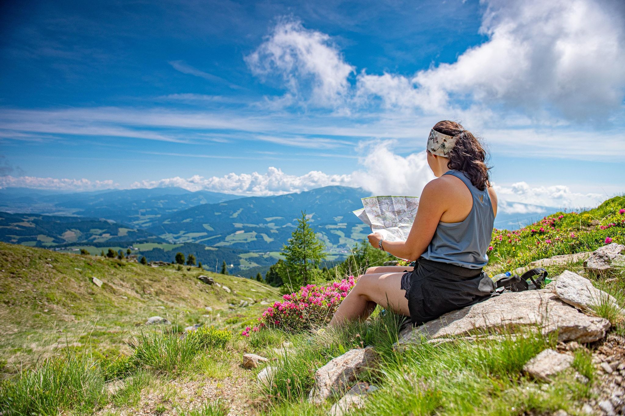 Une personne assise sur un rocher, une carte à la main, et qui contemple un paysage montagneux.