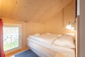 A wooden cabin room with a bed, a door with a glass panel, and a nightlight.