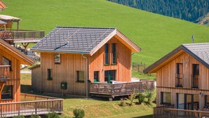 Eine Holzhütte mit Balkon, vor dem Hintergrund grüner Hügel und eines bewaldeten Berges.