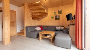 Ein modernes Interieur mit einer Wendeltreppe aus Holz, einem grauen Ecksofa, einem Holztisch und einem Flachbildfernseher.