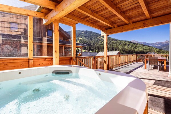A wooden deck with a hot tub, wooden railings, and a view of a mountainous landscape.