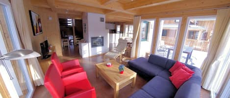Ein großzügiger Wohnbereich mit Holzboden, einer Couch, roten Sesseln, einem Couchtisch und einem Kamin.
