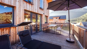 A wooden deck with outdoor furniture, including a table and chairs, and a large umbrella providing shade.