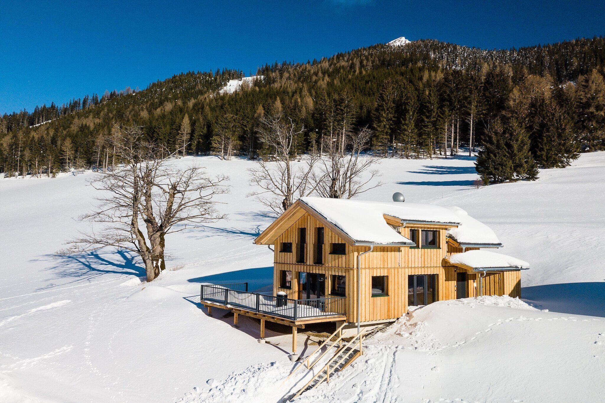 A wooden cabin with a balcony, surrounded by snow and trees.