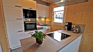 A modern kitchen with white cabinets, a built-in oven, a sink, and a window with a view of buildings outside.