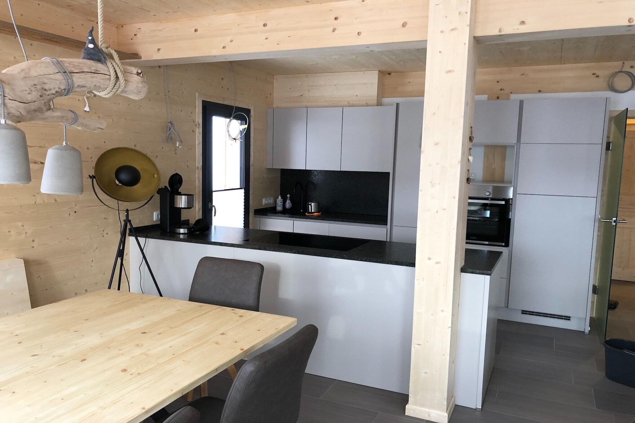 Une cuisine moderne avec des meubles blancs, un plan de travail noir et une table à manger en bois, accompagnée de chaises.