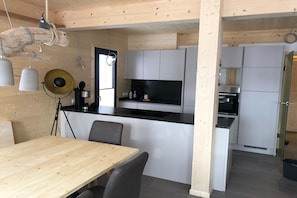 Ett modernt kök med vita skåp, en svart bänkskiva och ett matbord i trä med stolar.