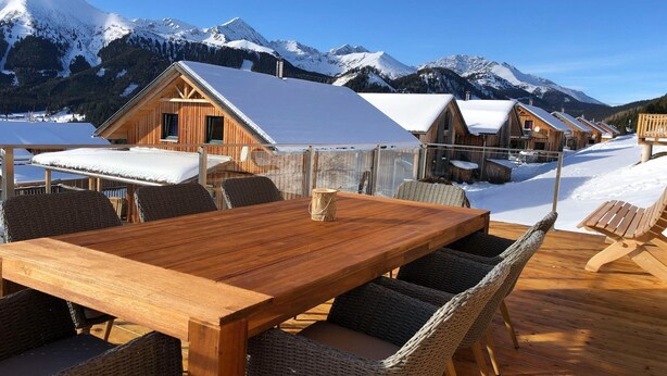 Een houten terras met een tafel en stoelen, omgeven door met sneeuw bedekte bergen.