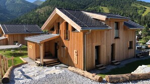 Een houten vakantiehuis met een schuin dak, een overdekte veranda en een bord waarop 'MIGLIONI HOME' staat.