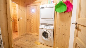 A laundry room with a front-loading washer and dryer, wooden walls, and a door with a diamond-shaped window.