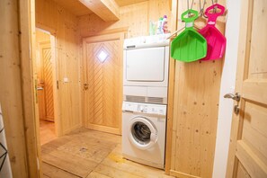 Une buanderie équipée d’un lave-linge et d’un sèche-linge à chargement frontal, avec des murs en bois et une porte ornée d’une fenêtre en forme de losange.