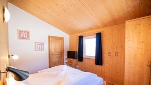 A wooden-paneled bedroom with a bed, a television on a shelf, and two doors.