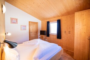 Une chambre à coucher aux murs lambrissés, avec un lit, un téléviseur posé sur une étagère et deux portes.