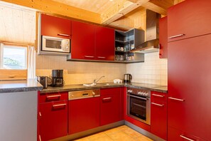 A kitchen with red cabinets, a microwave, a coffee maker, and an oven. - Chalet in Hohentauern with an outdoor hot tub (Hohentauern)
